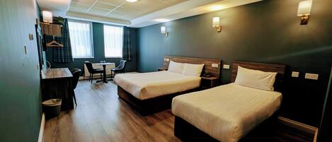 A hotel room with two beds, a desk with a chair, a small table, and a window with curtains.