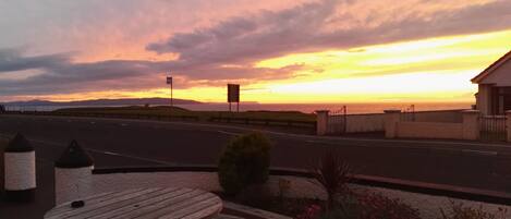 A sunset view from a roadside picnic table with a view of the ocean and distant mountains.