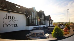 An Inn on the Coast Hotel with a white exterior, large windows, and outdoor seating area with tables and chairs.