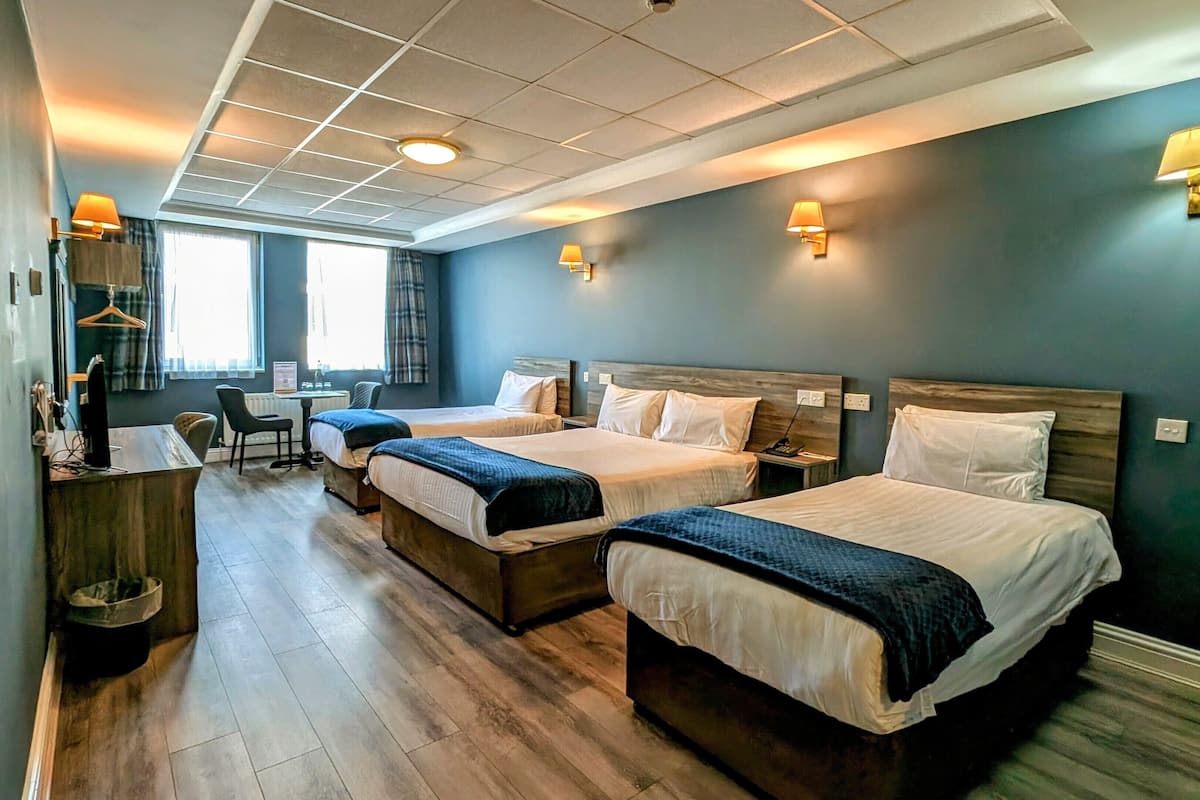 A hotel room with two beds, a desk, a chair, and a small table.