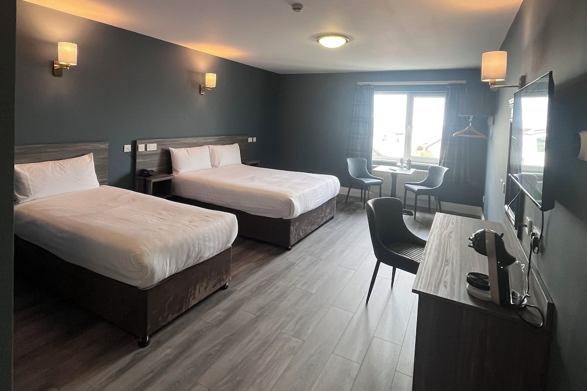 A hotel room with two beds, a desk, a chair, a TV, and a window.