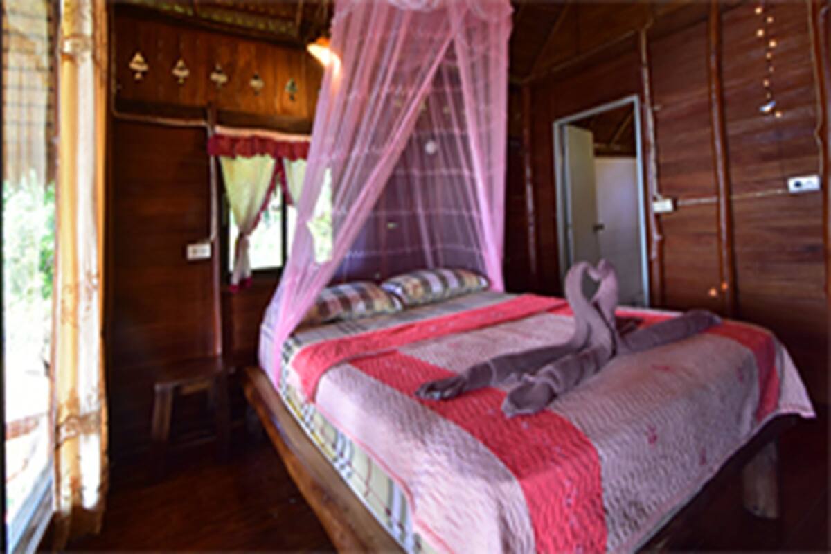 Um quarto de madeira com uma cama, um banco e uma cama com dossel.