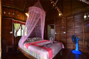 Ein Zimmer aus Holz mit einem Bett, einem Moskitonetz und einem Ventilator.