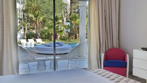 Un dormitorio con vistas a una piscina y un jardín, una cama, un aparador blanco y una silla roja.