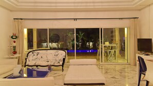 Amplio salón con un gran ventanal corredera que da a un espacio exterior con piscina y plantas tropicales.