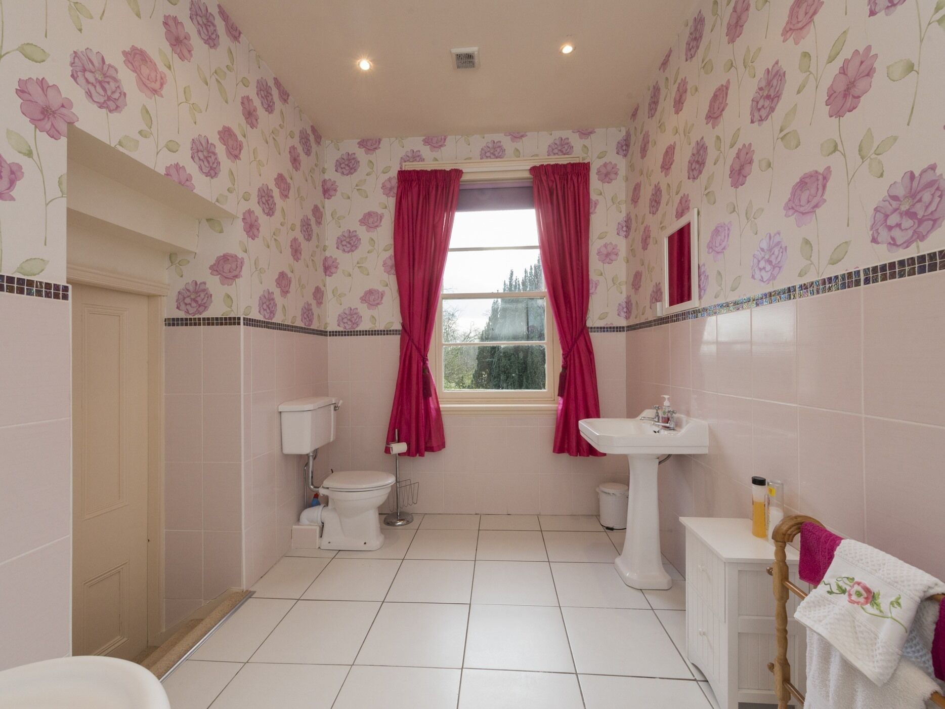 Un bagno con carta da parati a motivi floreali, un water, un lavabo e una finestra con tende.