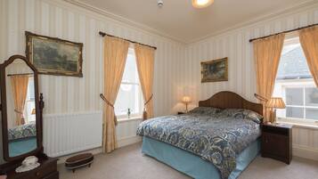 A bedroom with a large bed, two bedside tables, a dresser, a mirror, and a window with curtains.