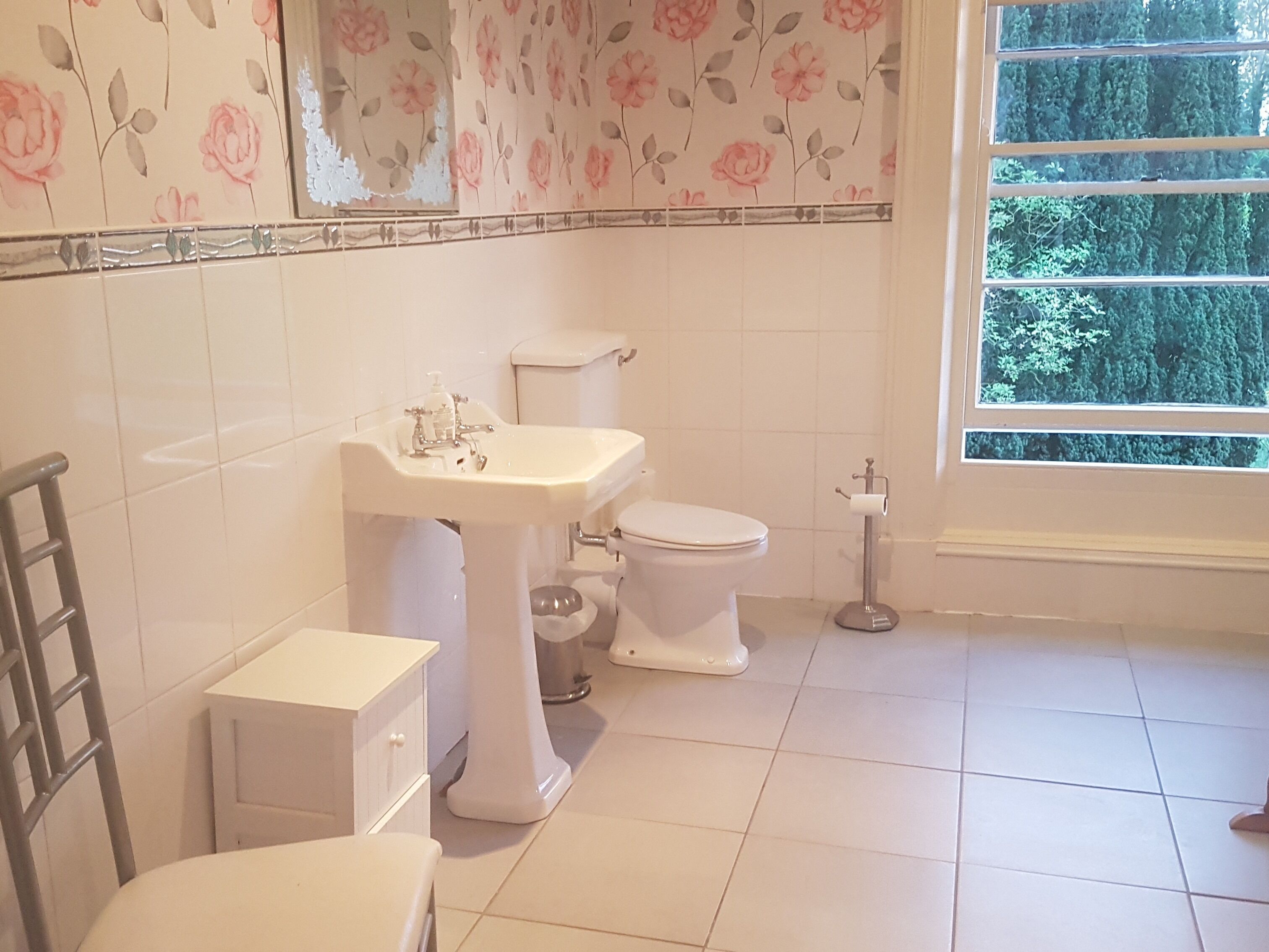 Ein Badezimmer mit Toilette, Waschbecken und einem Fenster mit Blick auf Bäume.