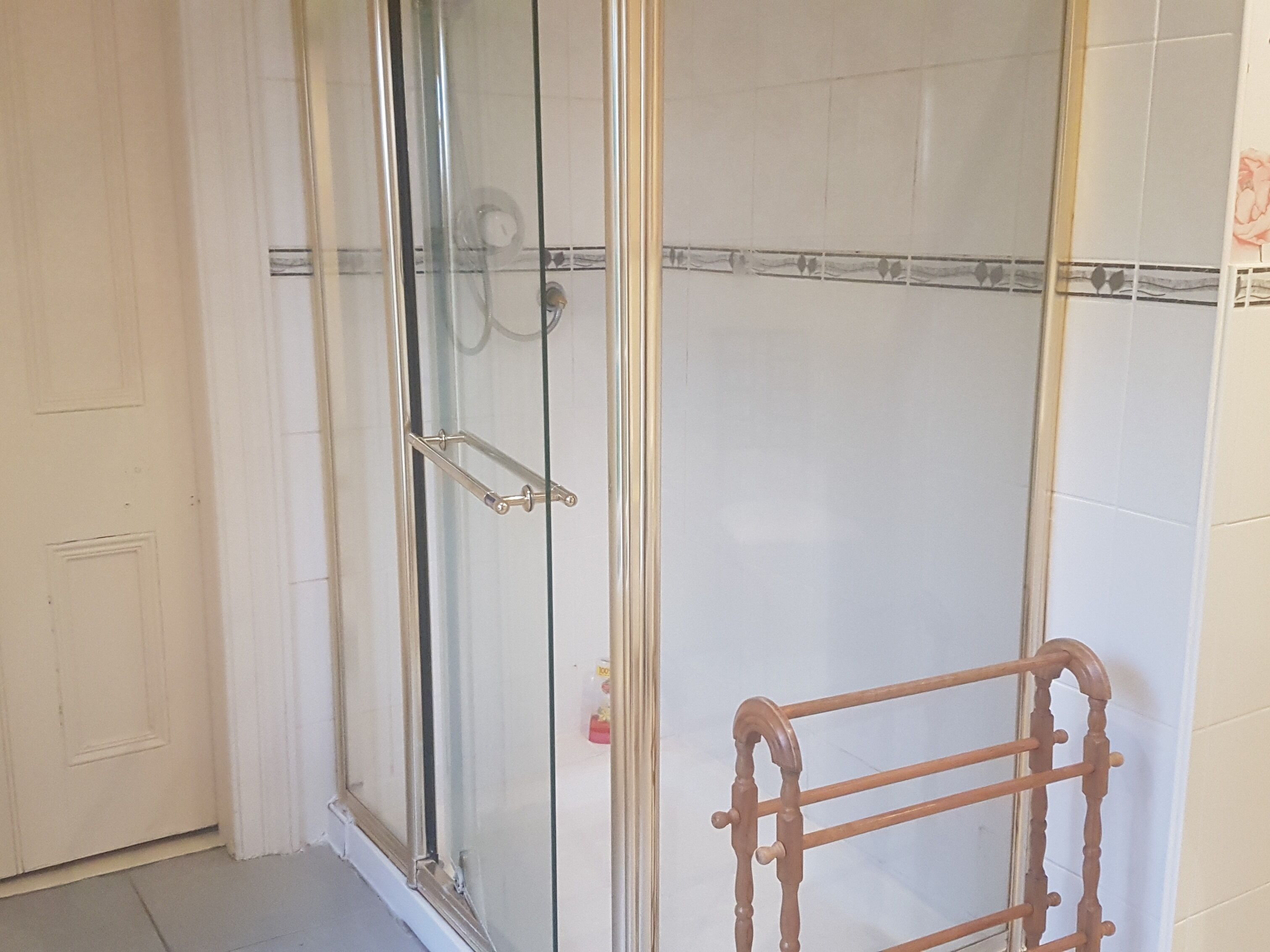 Un espace douche entièrement vitré, avec un porte-serviettes en bois.