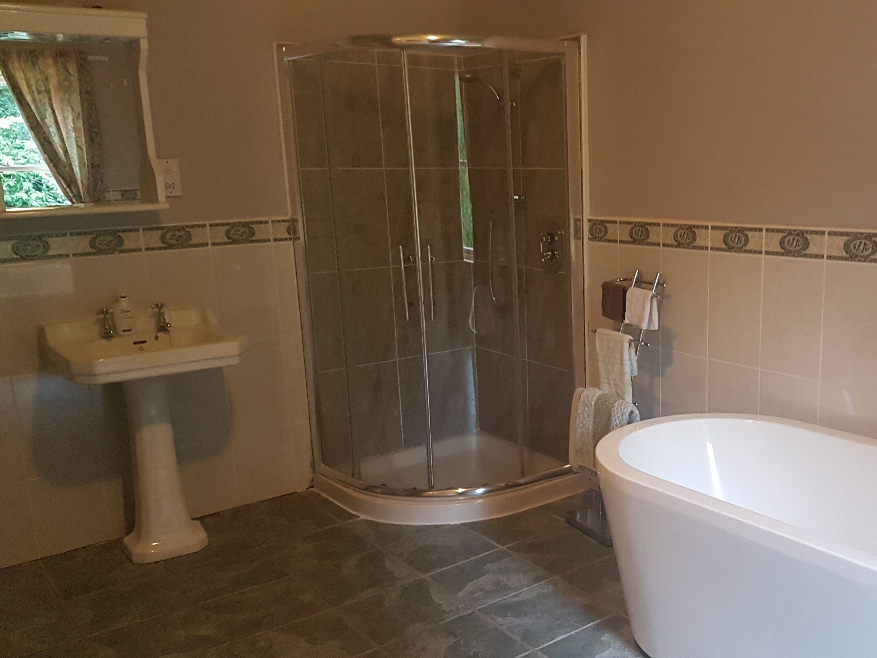 A bathroom with a glass-enclosed shower, a pedestal sink, and a freestanding bathtub.