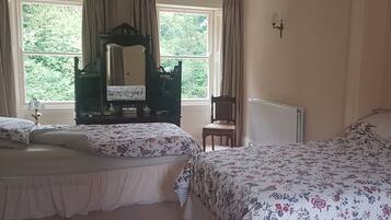 A bedroom with two beds, a dresser, a chair, and a window with curtains.
