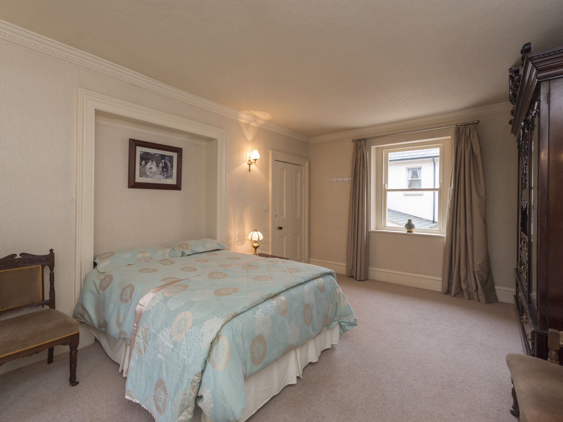 A bedroom with a bed, a chair, a dresser, a window with curtains, and a wall-mounted picture.