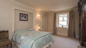 A bedroom with a bed, a chair, a dresser, a window with curtains, and a wall-mounted picture.