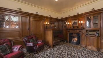 Uma biblioteca tradicional com poltronas de couro, lareira e estantes de madeira.