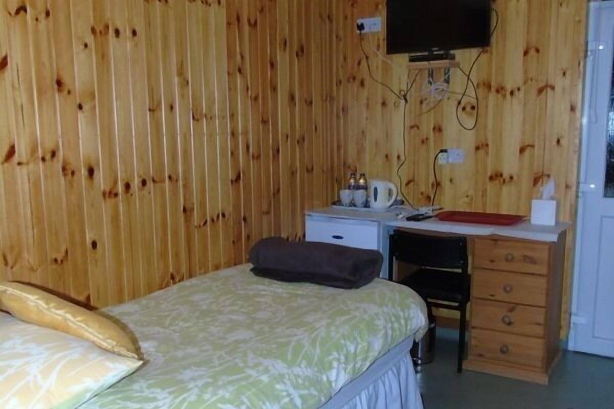 A room with a bed, a desk with a chair, a television mounted on the wall, and a small kitchenette area.