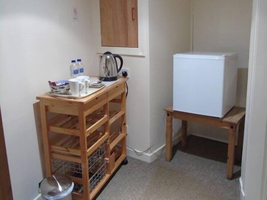 A small kitchenette with a wooden cart, a white refrigerator, and a kettle on the counter.