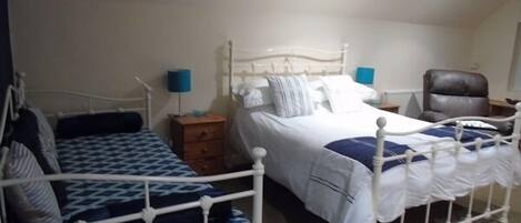 A bedroom with two beds, a chair, a nightstand, and a lamp.
