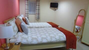 A bedroom with two beds, a bedside table with a lamp, a TV mounted on the wall, and a mirror.