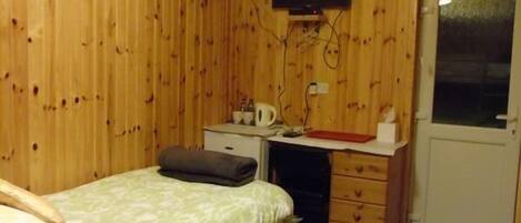 A small, cozy room with a bed, a desk, a chair, and a television mounted on the wall.