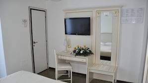 Quarto de hotel com uma cama, uma escrivaninha com cadeira, uma televisão e um espelho.
