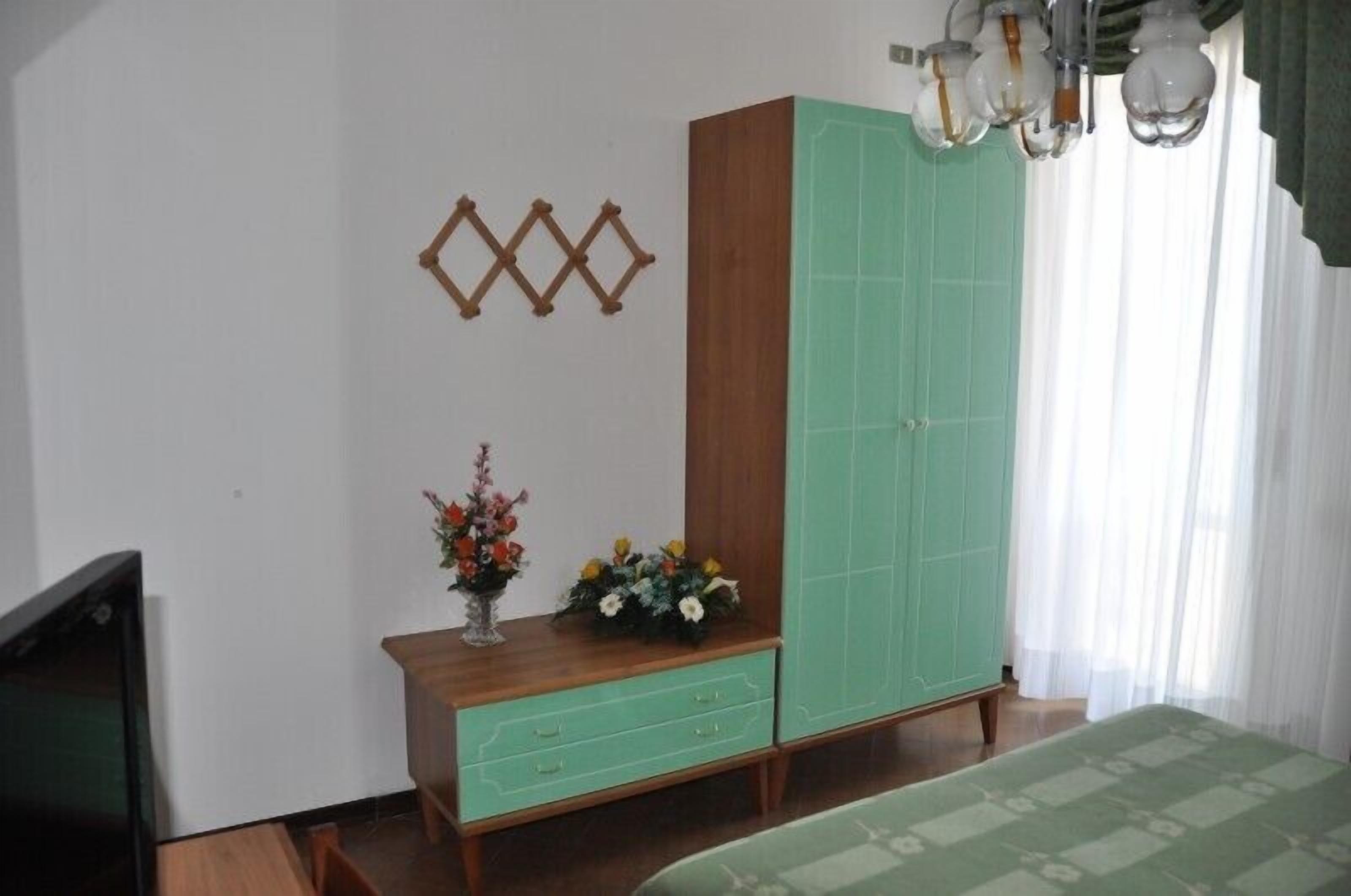 Una camera da letto con un letto, un armadio verde, una cassettiera in legno, un faretto a parete e un elemento decorativo.
