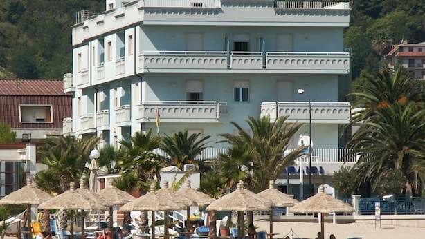 Um hotel com vários andares e vista para a praia, com área de estar externa e guarda-sóis.