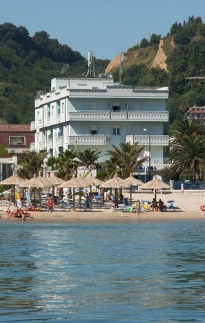 Een meerlaags hotel met uitzicht op het strand, voorzien van terrasmeubels en parasols.
