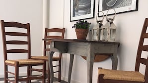 Un comedor con suelo a cuadros, una mesa de madera y cuatro sillas de madera. Hay dos cuadros en la pared.