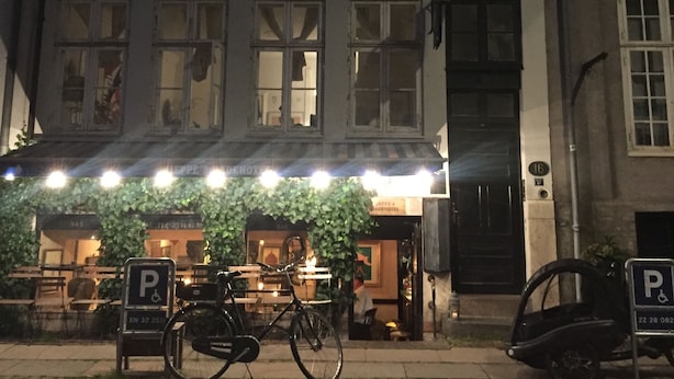 Un edificio con varias ventanas, un letrero que anuncia un bar y una bicicleta estacionada adelante.