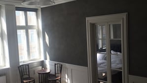 Un dormitorio con una cama grande, una mesita con sillas, un ventilador de techo y una puerta que da a otra habitación.