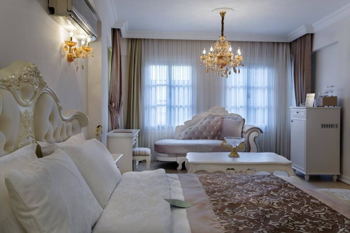 A bedroom with a large bed, a chaise lounge, a small table, and a chandelier.