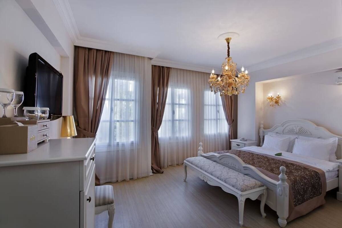 A hotel room with a bed, bedside table, lamp, TV, and curtains.