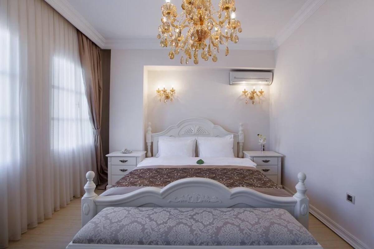 A bedroom with a large bed, two bedside tables, a chandelier, and an air conditioning unit.