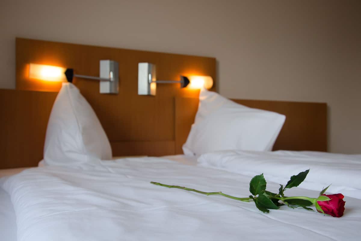 A neatly made bed with white linens, a wooden headboard, and two wall-mounted light fixtures.