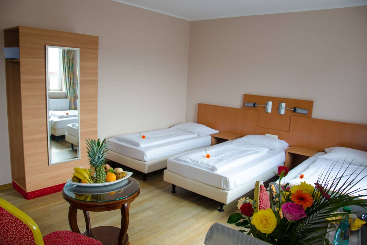 A hotel room with two single beds, a wooden wardrobe, a small round table with a fruit bowl, and a mirror.