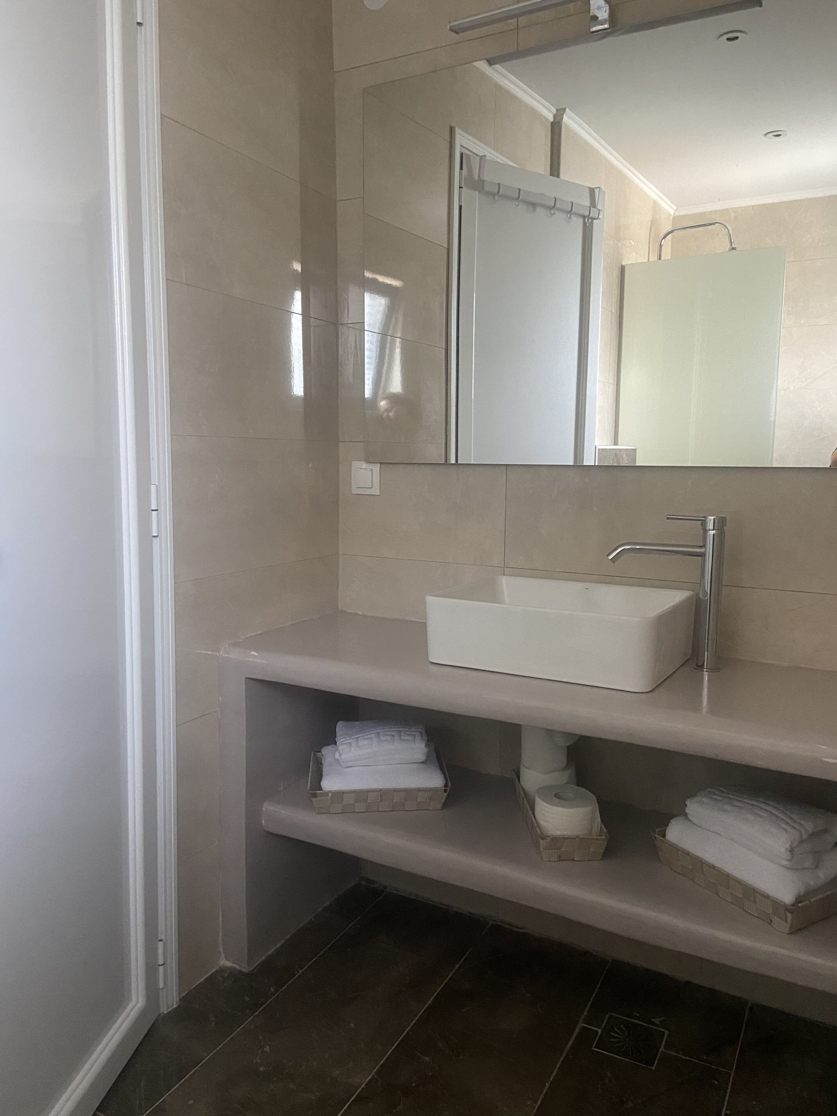 Un baño moderno con un lavamanos blanco, un espejo y un estante con toallas dobladas.