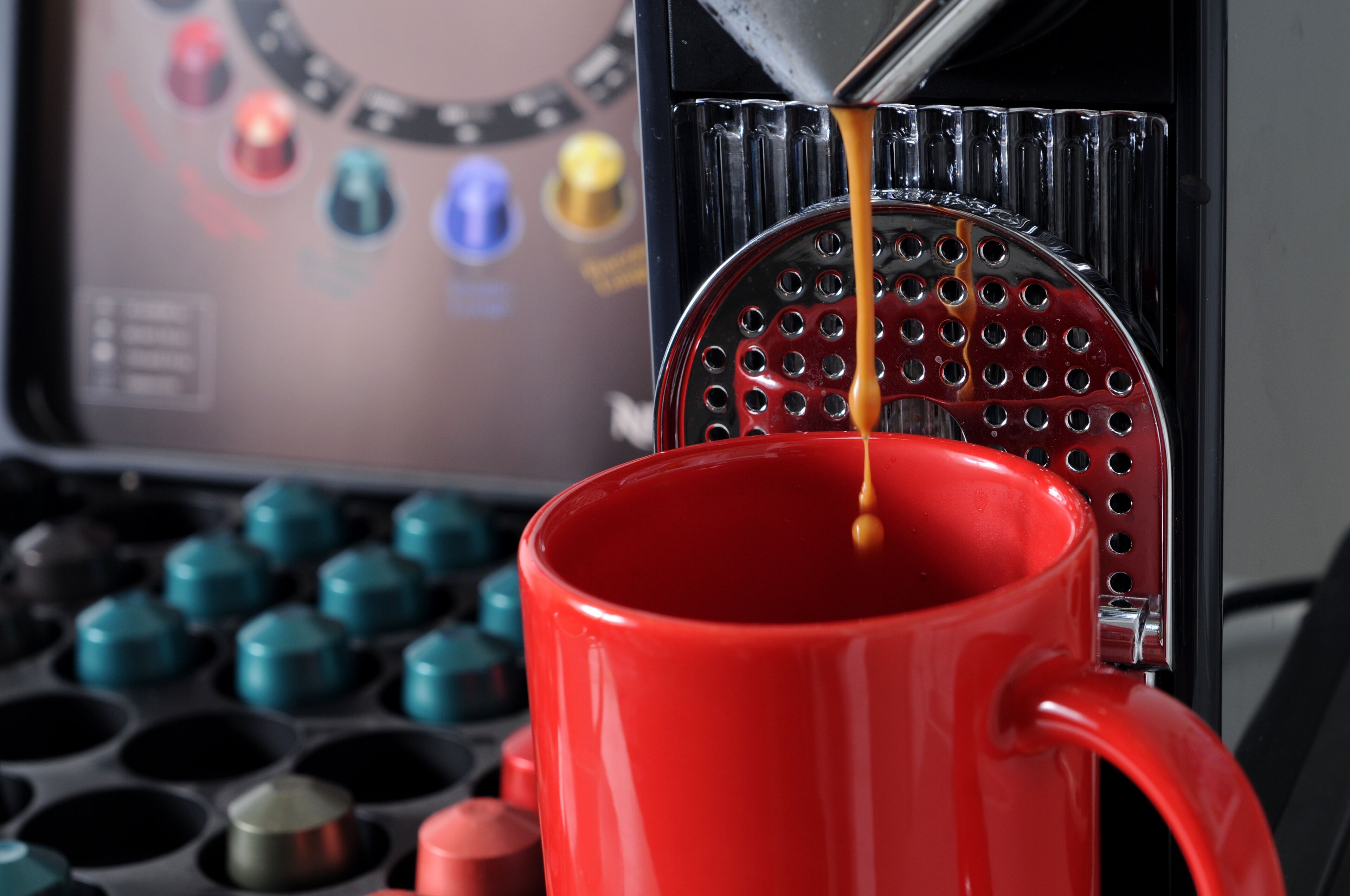 A red coffee cup with a metal strainer and a coffee machine in the background.