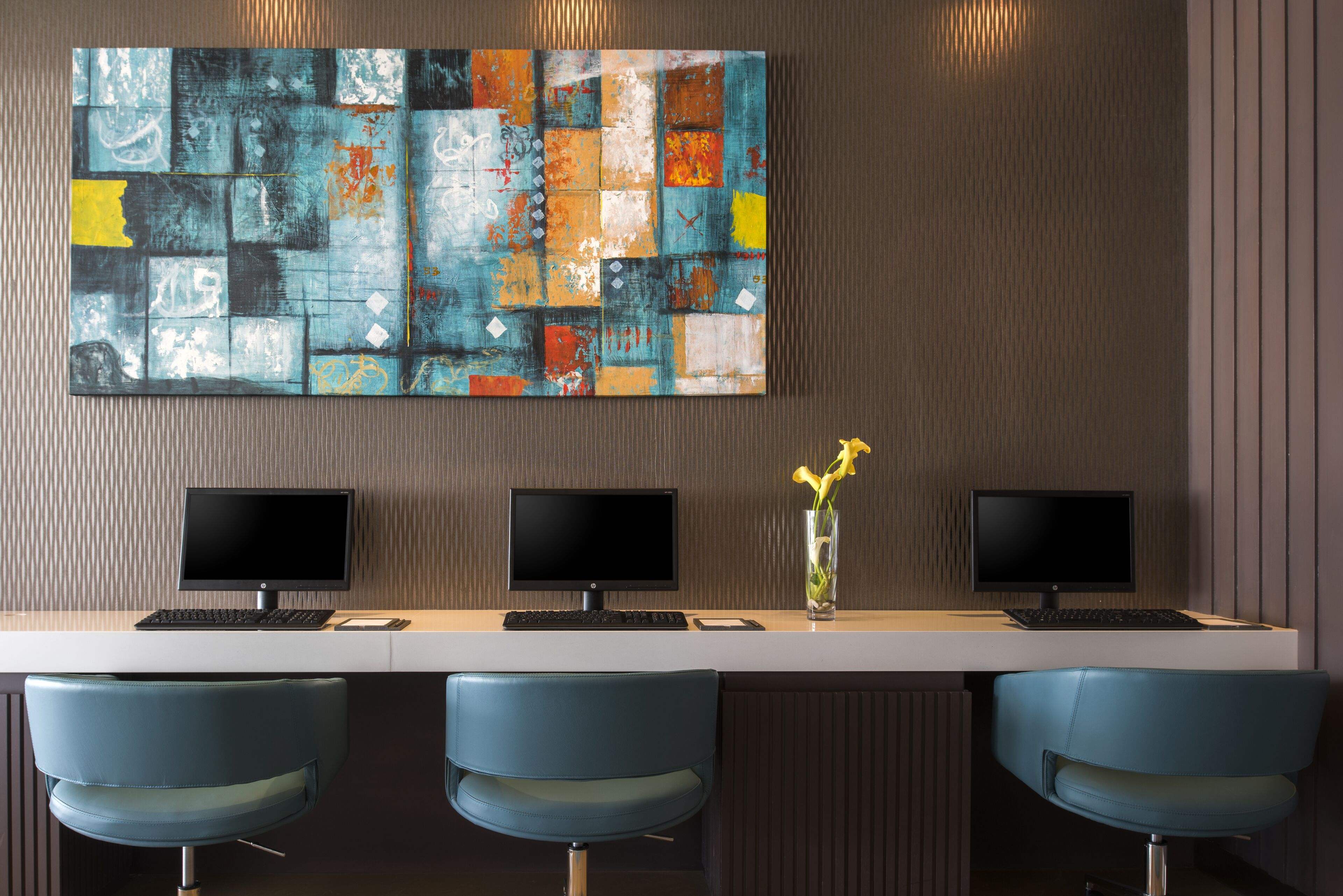 A modern office space with three monitors, a white desk, and three blue chairs.