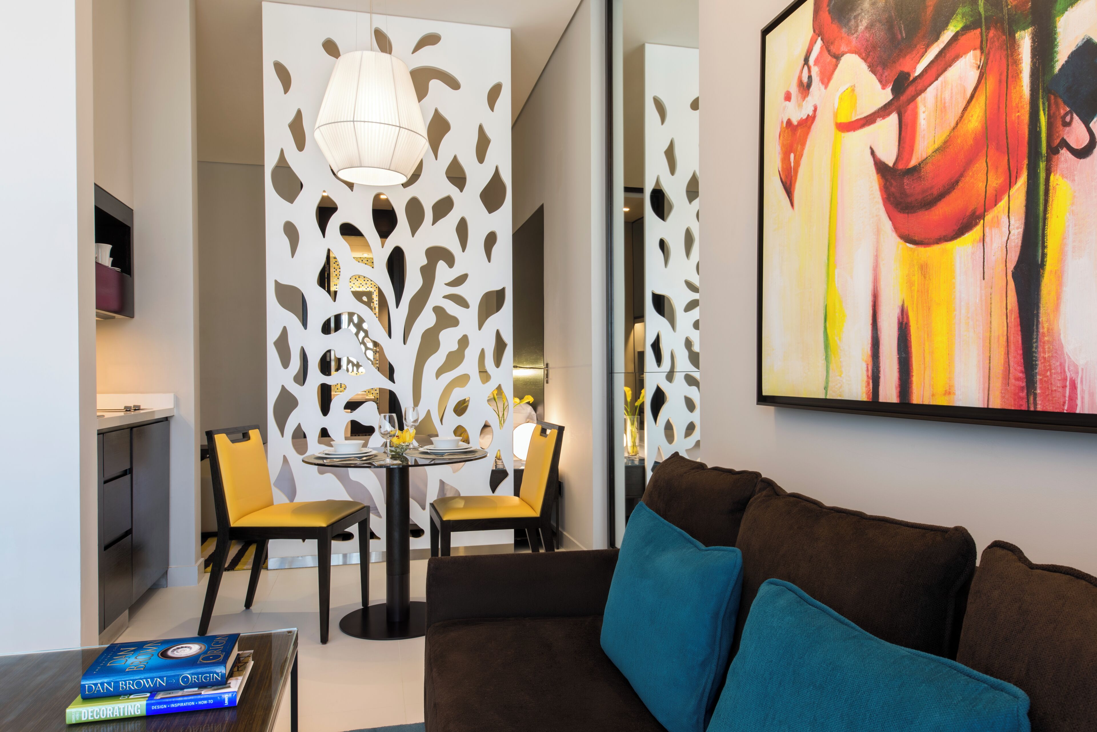 Una sala de estar moderna con un sofá marrón, una mesa de comedor con sillas, un separador decorativo y un cuadro en la pared.