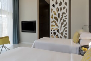 A modern hotel room with two beds, a TV mounted on the wall, a decorative partition, and a yellow chair.