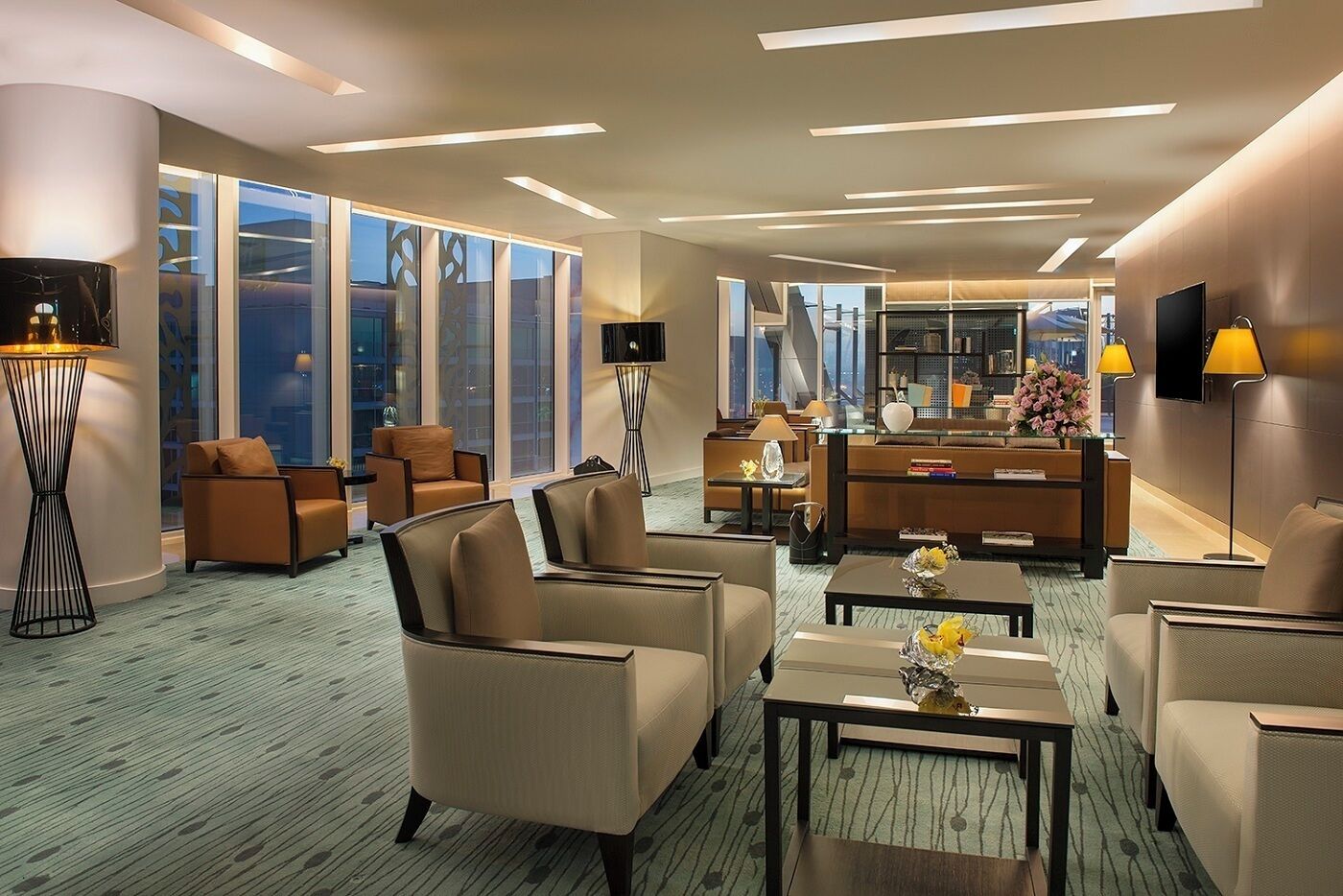 Un moderno vestíbulo de hotel con zona de estar, una recepción y ventanas grandes con vistas a la ciudad.