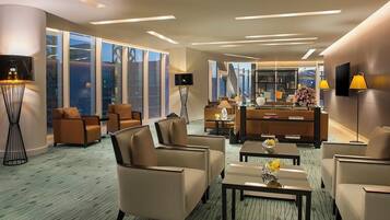 A modern hotel lobby with a seating area, a reception desk, and large windows offering a city view.