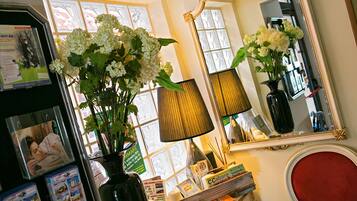 A room with a large mirror, a vase with white flowers, a lamp, and a window with blinds.