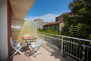 A balcony with a table and two chairs, surrounded by a white railing and greenery. - Hotel Lo Squalo (Grottammare)