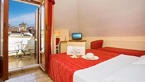 Habitación de hotel con cama, escritorio con computadora, una silla y vista a la ciudad a través de una puerta de vidrio.