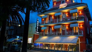 Un hotel de varios pisos con balcones, mobiliario exterior y un letrero que indica que es un hotel.