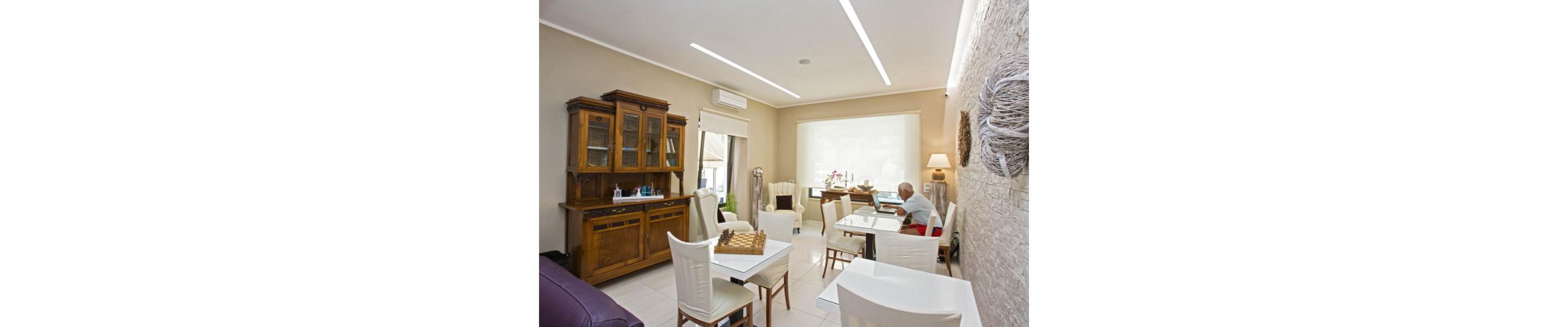 A spacious room with a large wooden cabinet, a dining table with chairs, and a white sofa.