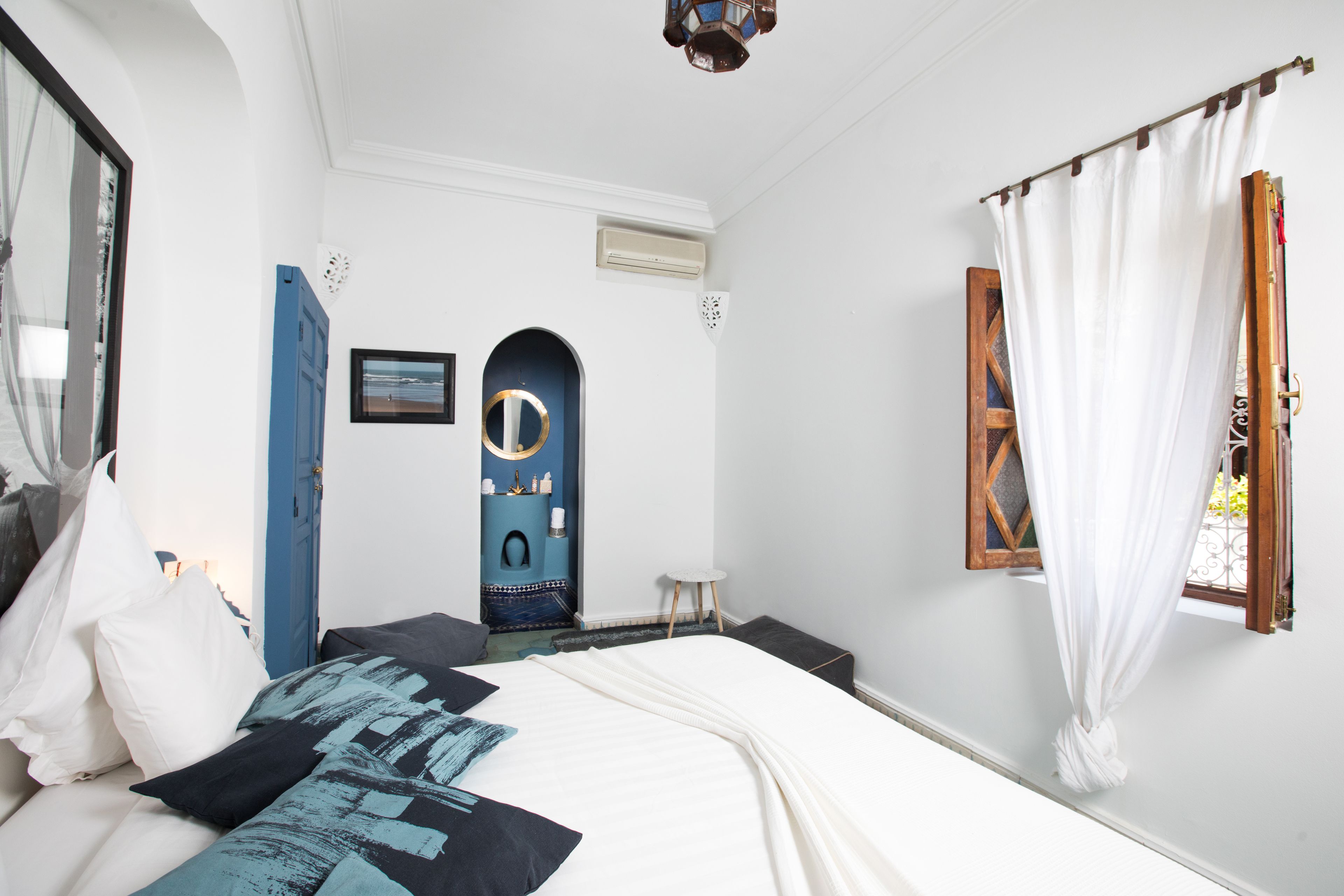 A bedroom with a bed, a window with curtains, a door, and a wall-mounted air conditioner.