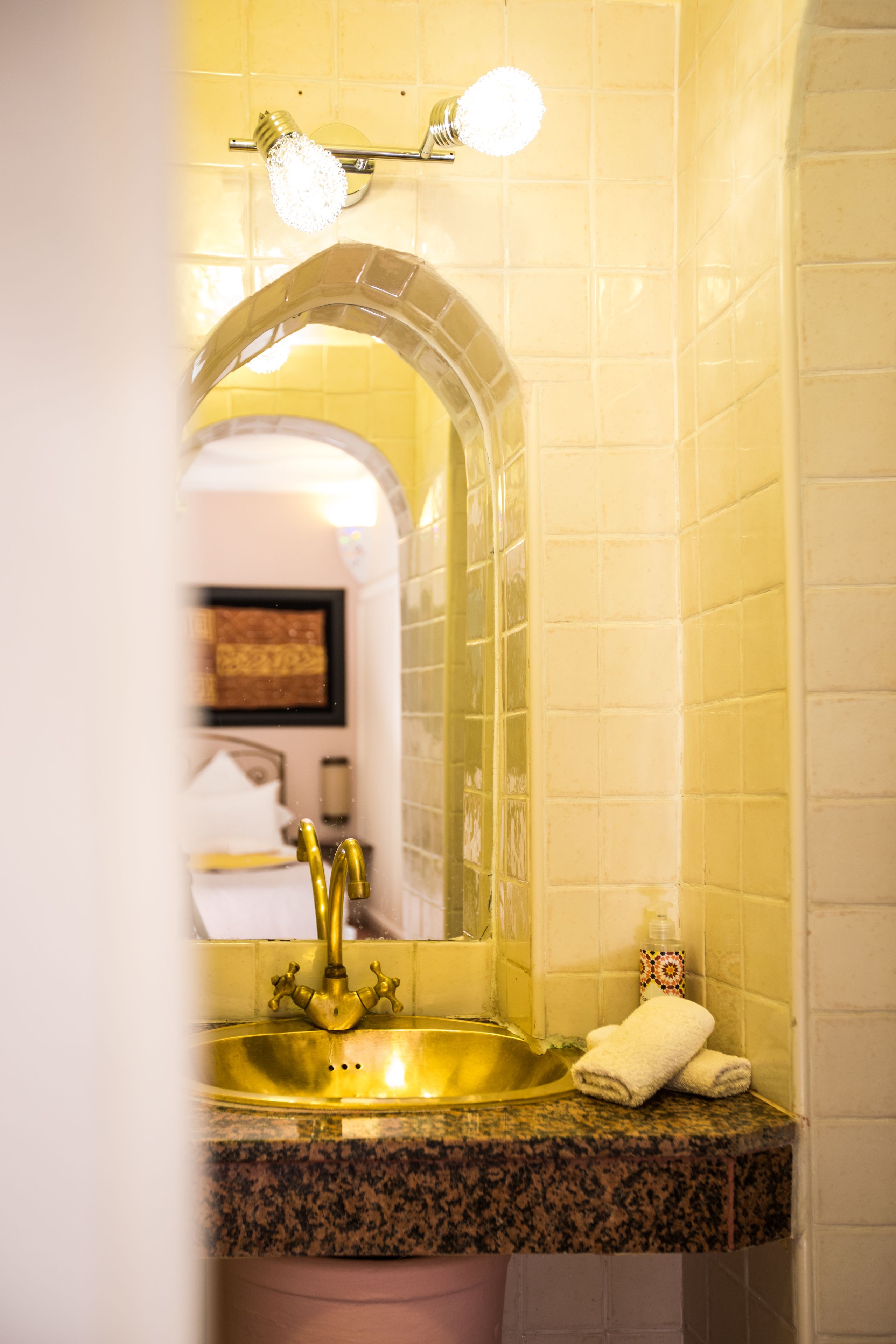 A bathroom with a gold sink, a mirror, and a towel rack.
