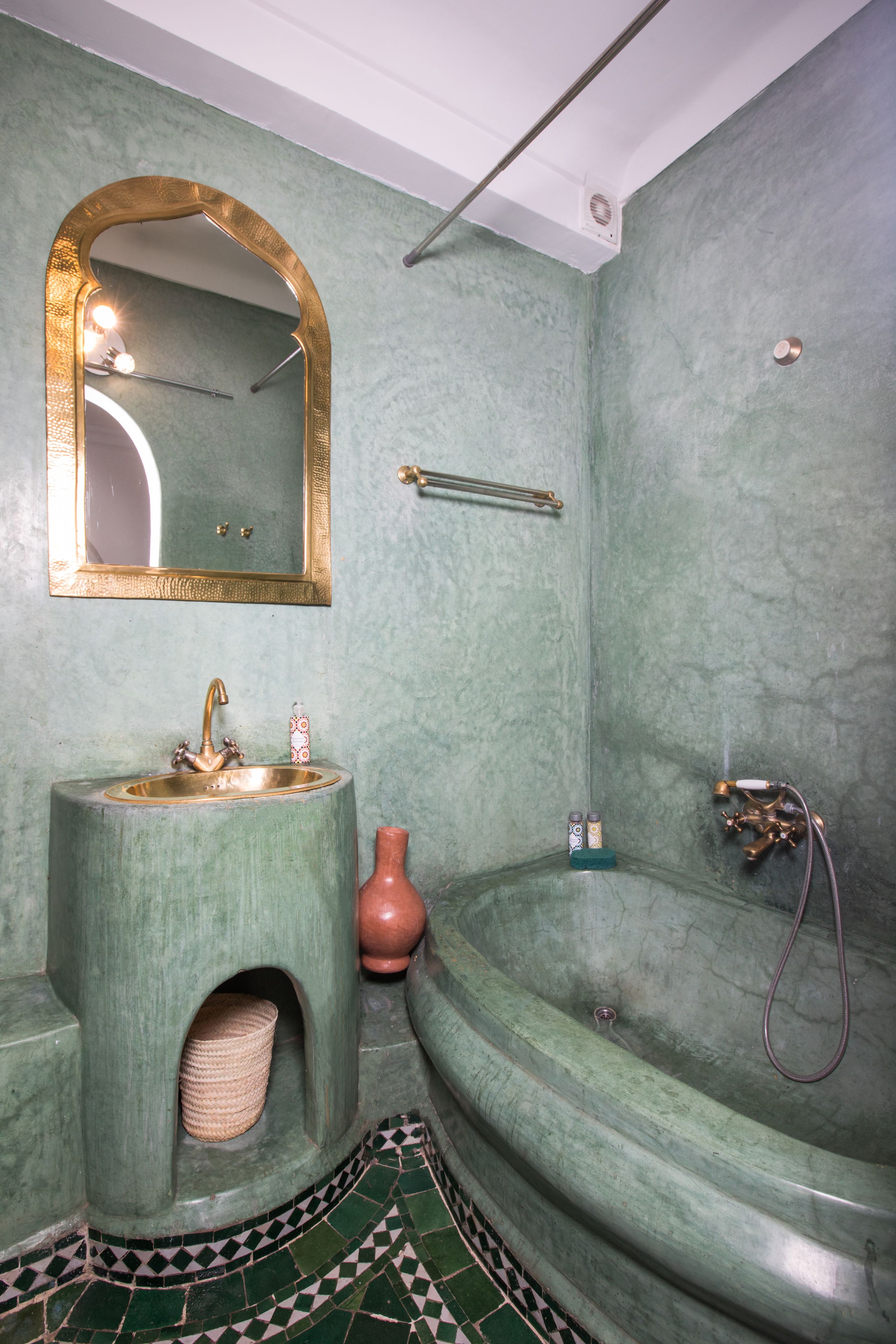 Un baño con un lavabo verde, un espejo con marco dorado, una bañera y suelo de baldosas.